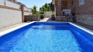 Ein rechteckiger Swimmingpool mit blauen Fliesen, umgeben von einer Ziegelmauer und einem weißen Zaun.