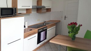 A compact kitchen with white cabinets, a microwave, a stove, and a sink. There is a wooden table with a vase of red flowers.