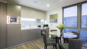 A modern kitchen with a microwave, oven, and sink. There is a dining table with chairs and a vase with flowers.