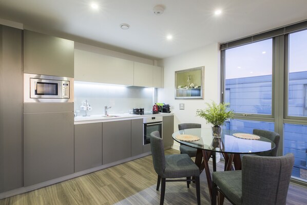 A modern kitchen with a microwave, oven, and sink. There is a dining table with chairs and a vase with flowers.