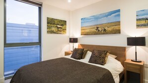 A bedroom with a large bed, two nightstands, a window, and three wall-mounted paintings.