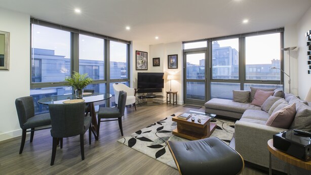 A modern living room with a sofa, chairs, a coffee table, a TV, and large windows offering a city view.