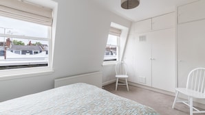 A bedroom with a bed, two windows, a radiator, a wardrobe, and a chair. - JOIVY Pimlico Flat with Terrace for 3 (London)