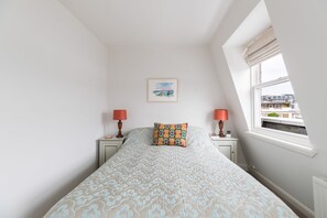 Een slaapkamer met een bed, twee nachtkastjes met lampen, een raam met uitzicht en een fotokader aan de muur.