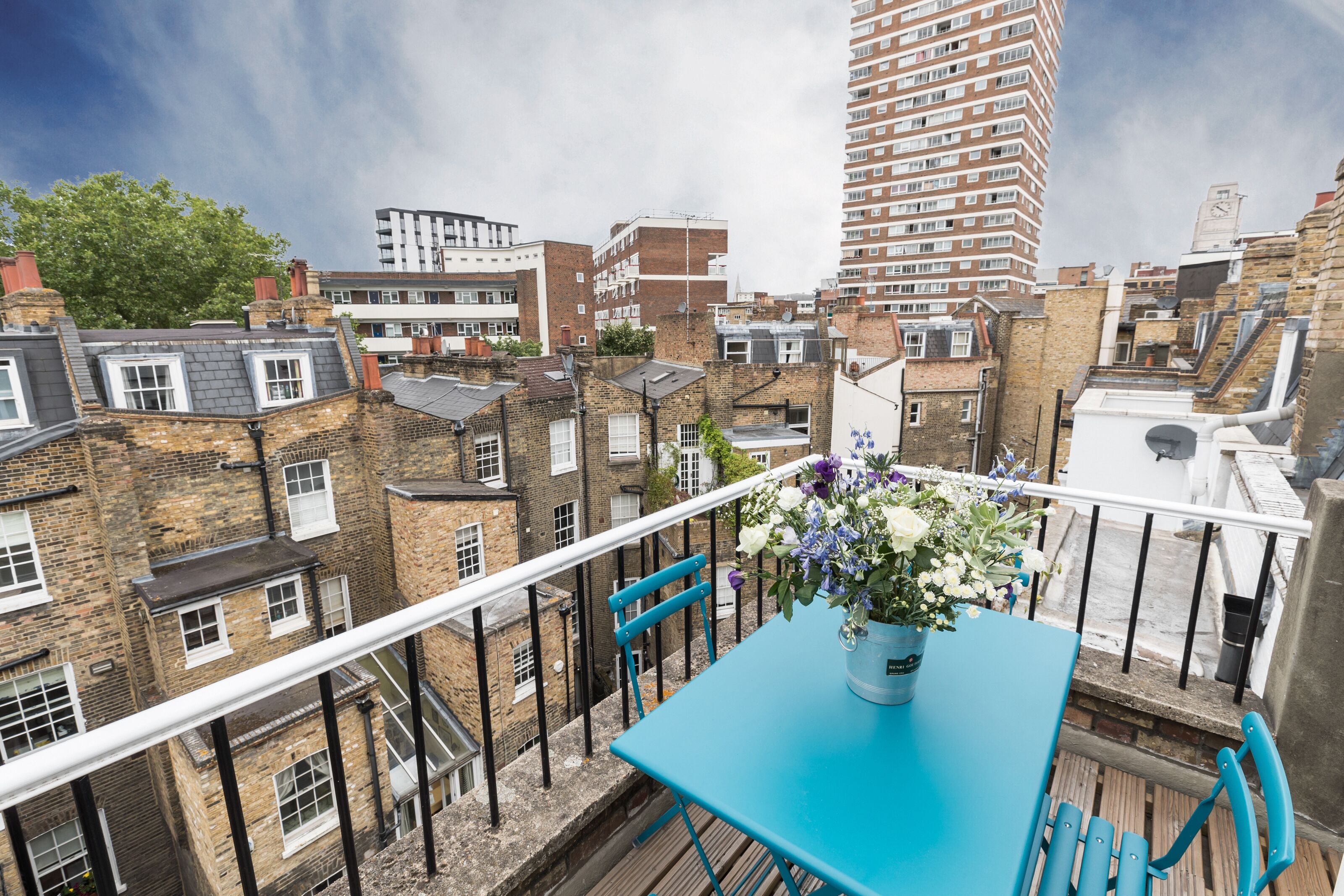 Un balcon avec une table et des chaises bleues, donnant sur un paysage urbain composé de différents bâtiments.