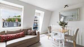 A living room with a sofa, chairs, a dining table, and a large window with a view of buildings. - JOIVY Pimlico Flat with Terrace for 3 (London)