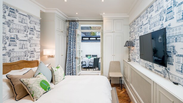 A bedroom with a bed, pillows, a TV, and a view of an outdoor dining area.