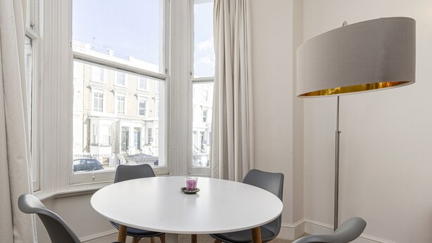 A round table with six chairs in a room with large windows and a floor lamp. - JOIVY Charming 1 Bed Flat, Sleeps 4 (London)