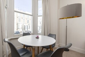 Une table ronde entourée de six chaises, dans une pièce dotée de grandes fenêtres et d’un lampadaire.