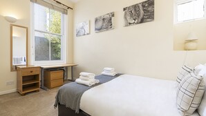 A bedroom with a bed, a desk, a chair, a window, and three wall-mounted pictures. - JOIVY Charming 1 Bed Flat, Sleeps 4 (London)