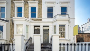 A multi-story townhouse with a front entrance, a set of stairs leading to the door, and a black metal fence surrounding the property. - JOIVY Charming 1 Bed Flat, Sleeps 4 (London)