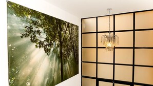 A room with a large wall-mounted painting of a forest scene, a grid-patterned partition, and a hanging chandelier. - JOIVY Splendid 1 Bedroom Flat near St. Paul's Cathedral (London)
