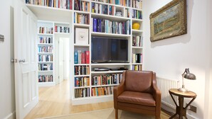 Une pièce avec une bibliothèque, un fauteuil en cuir marron, une petite table avec une lampe et un tableau encadré au mur.