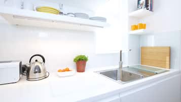A modern kitchen with white countertops, a stainless steel kettle, a small potted plant, and neatly arranged dishes on shelves.