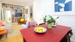 Un salon avec une table à manger rouge, une bibliothèque, un téléviseur et une plante en pot.