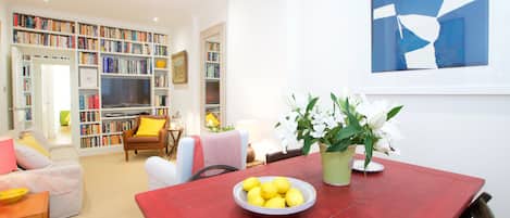 Ein Wohnzimmer mit einem roten Esstisch, einem Bücherregal, einem Fernseher und einer Topfpflanze.