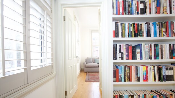 Un couloir avec une bibliothèque, une porte et une fenêtre équipée de stores.