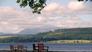 A lakeside view with three wooden chairs facing the water, surrounded by lush greenery and hills in the background. - Bunchrew House Hotel (Inverness)