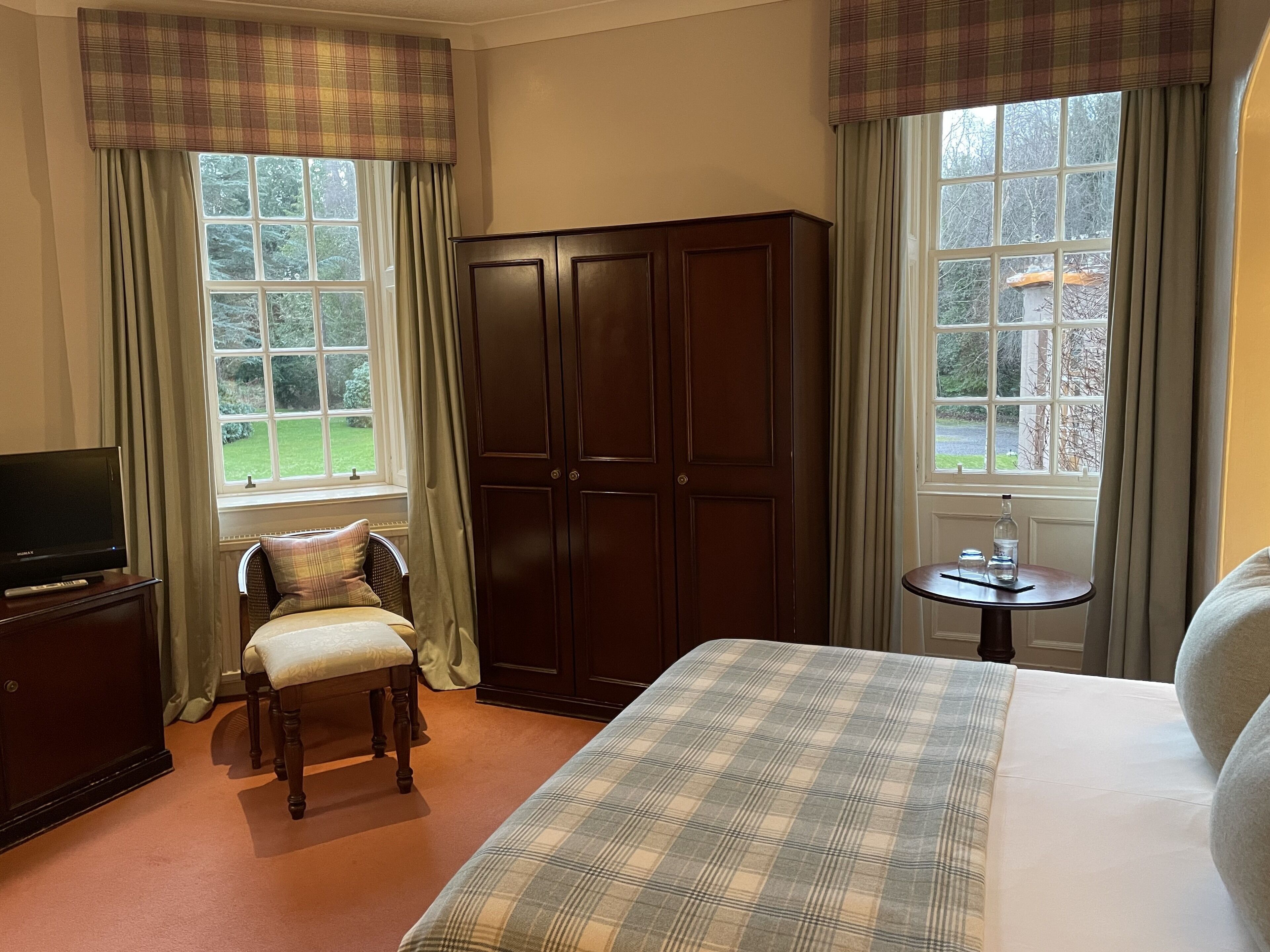 A hotel room with a bed, a television, a wardrobe, a chair, and a small table.
