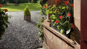 A porch with a gravel pathway, a doormat, and a window with red flowers. - Bunchrew House Hotel (Inverness)