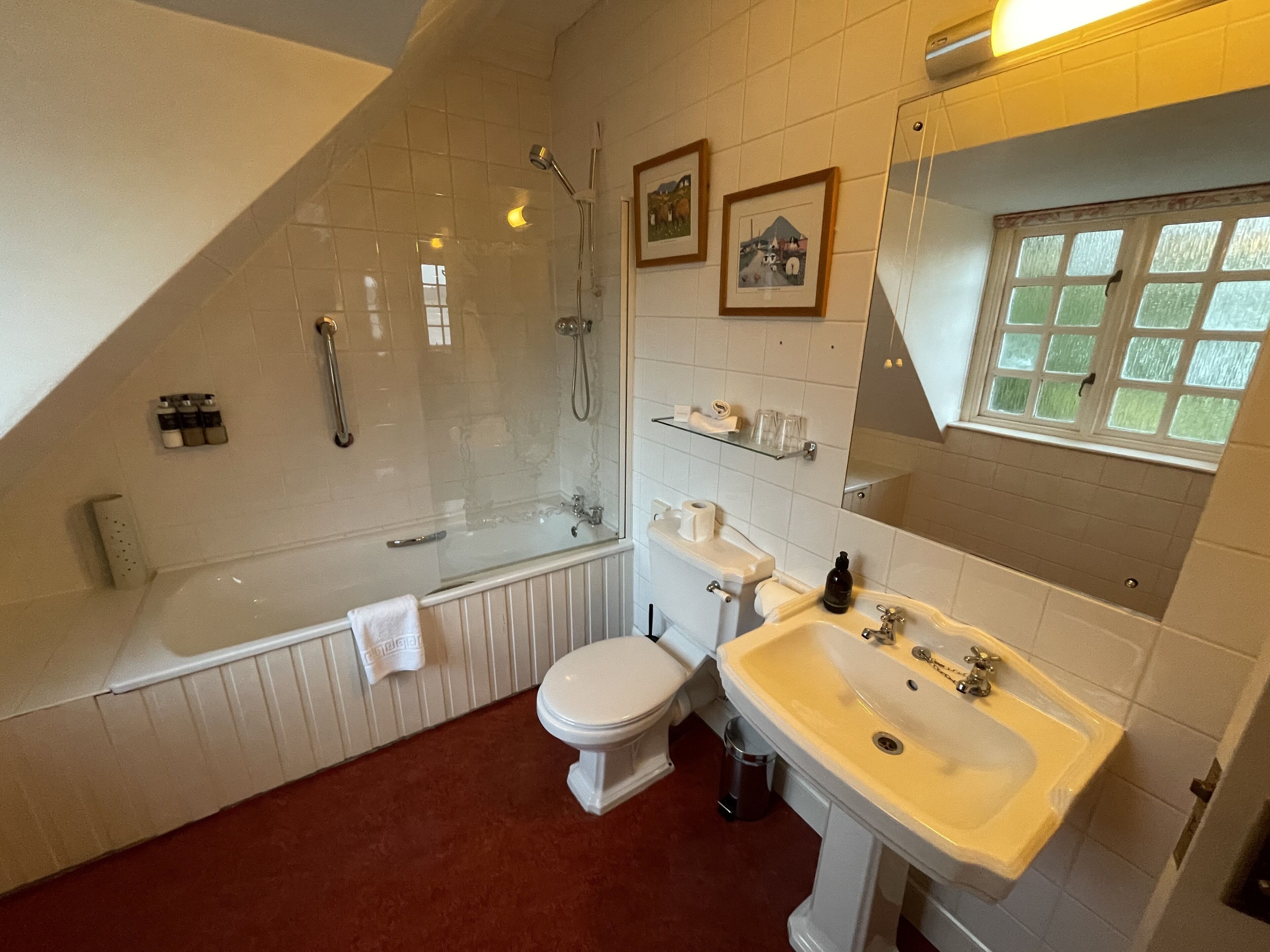 Een badkamer met bad, toilet en wastafel, met witte sanitair en een betegelde vloer.