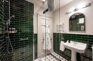 Un baño moderno con azulejos verdes y blancos, cabina de ducha de vidrio, lavabo blanco y espejo con revoque de azulejos verdes.