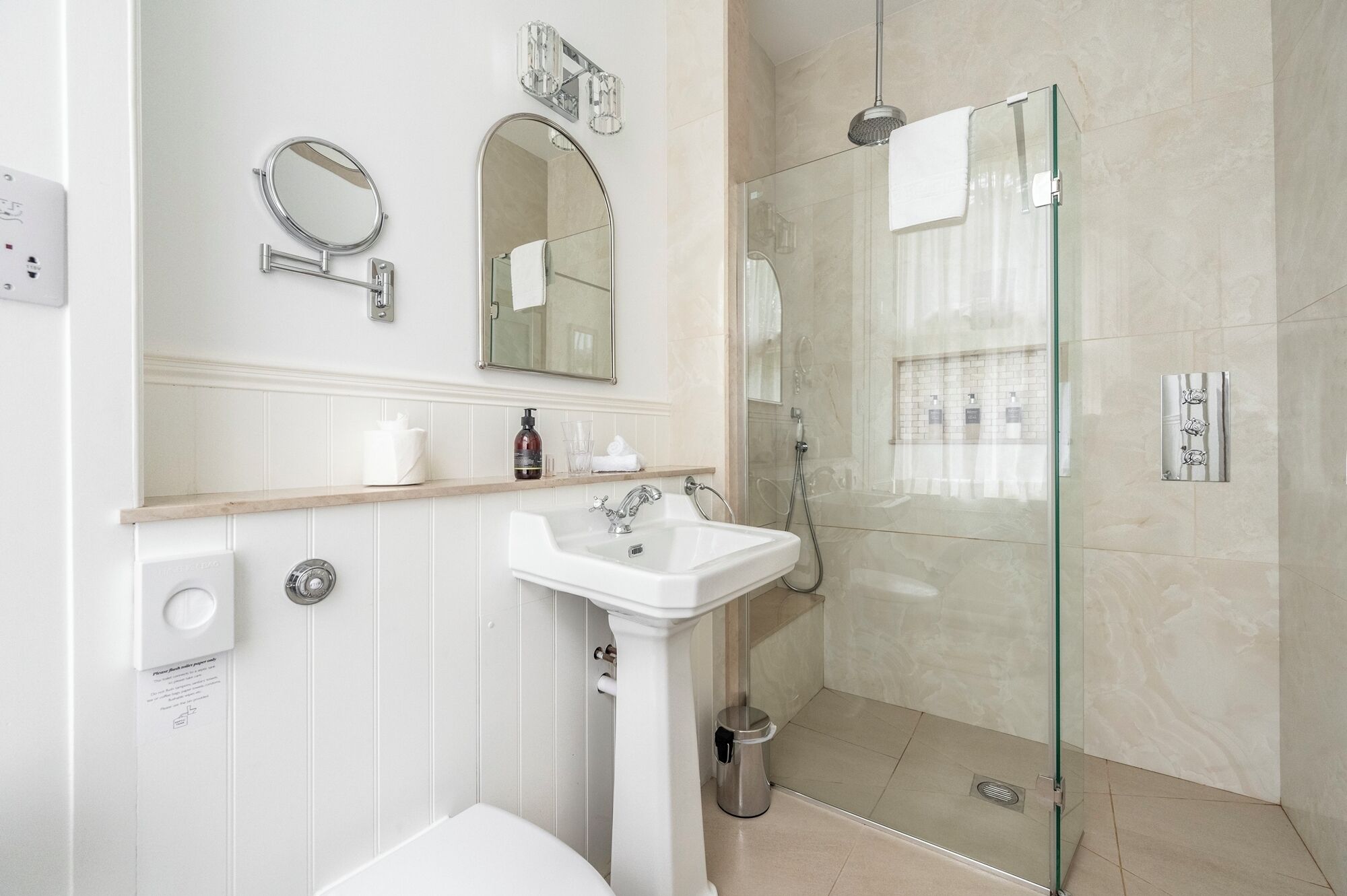 Une salle de bain moderne avec une douche à parois de verre, un lavabo sur colonne et deux miroirs fixés au mur.