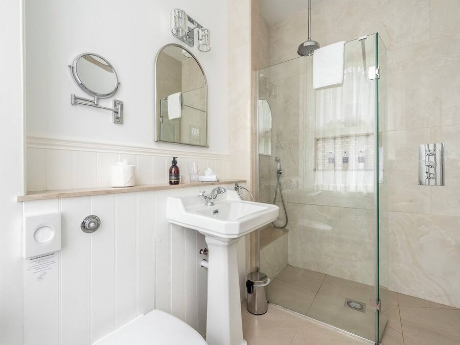 A modern bathroom with a glass-enclosed shower, a pedestal sink, and two wall-mounted mirrors.