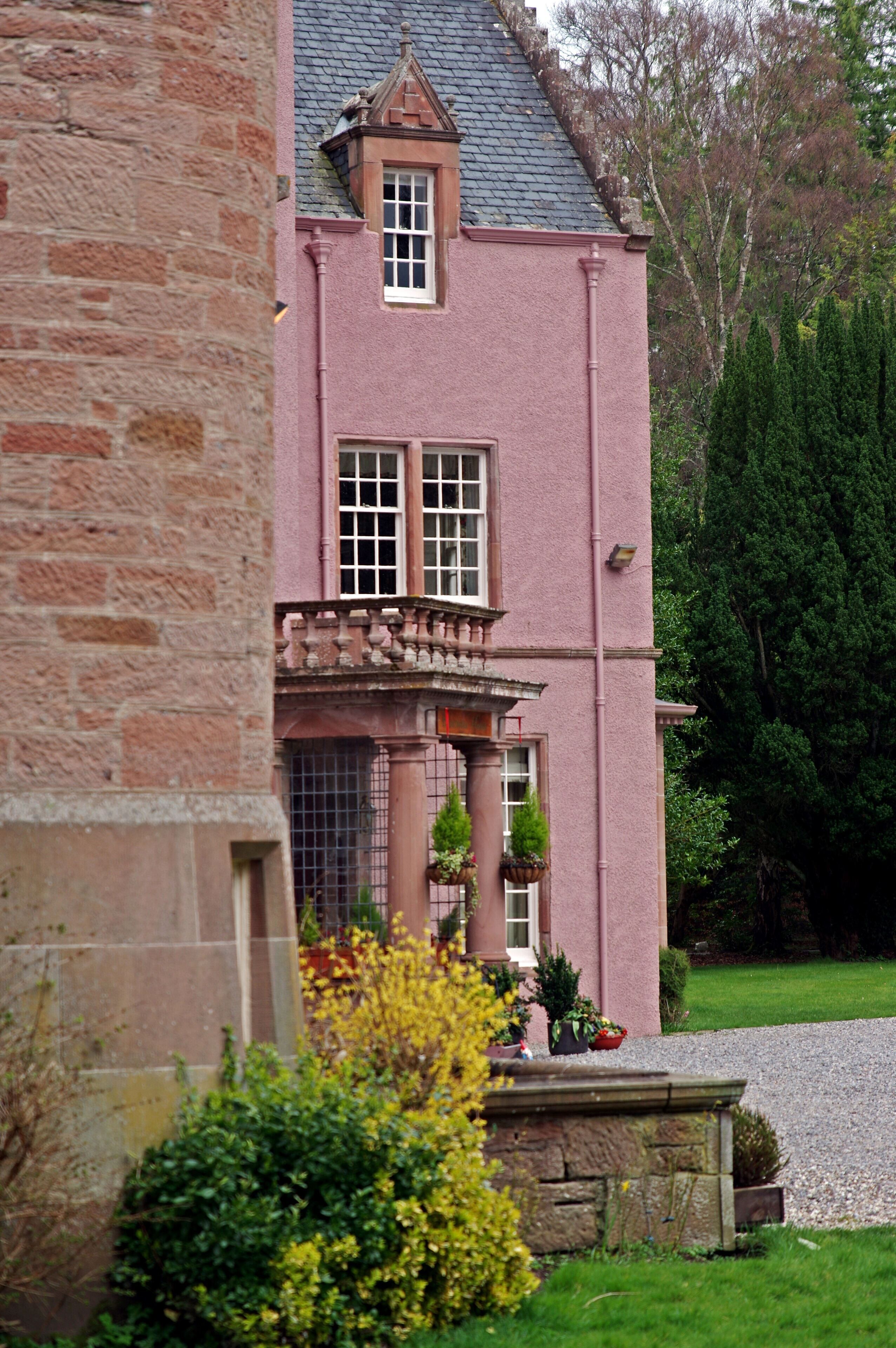 A pink building with a stone facade, a balcony with railings, and a window with a white frame.
