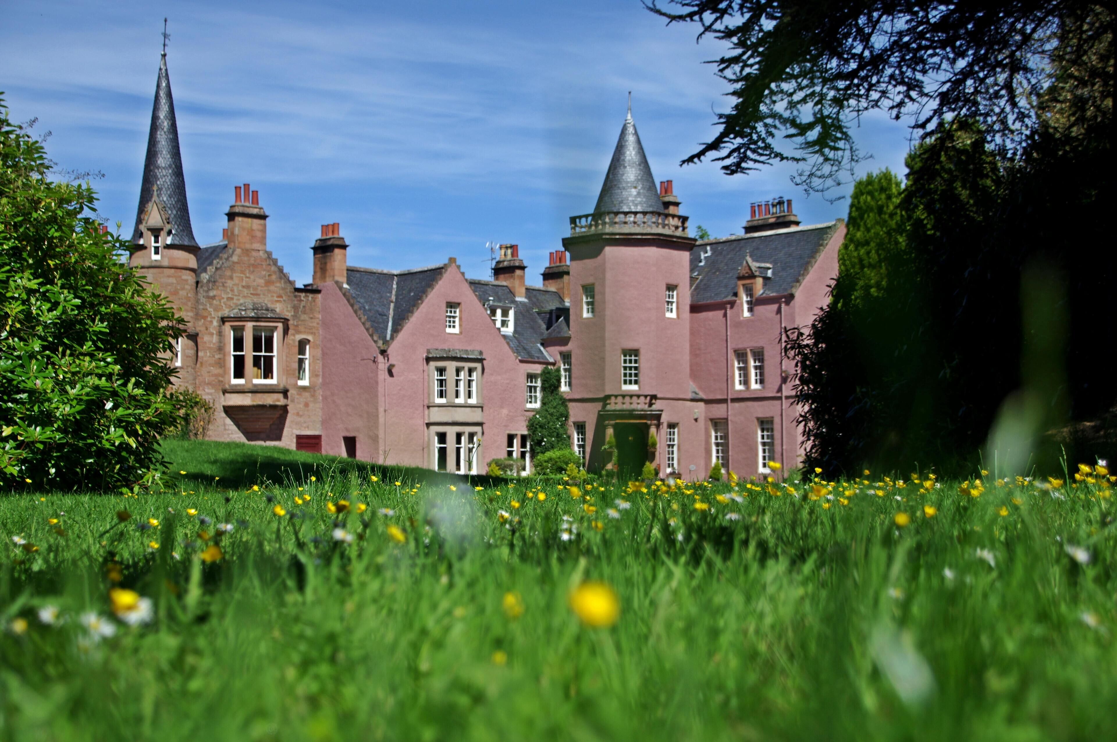 A historic building with multiple towers and a well-maintained garden with dandelions.