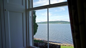 A room with a large window overlooking a lake, a stone wall, and a door. - Bunchrew House Hotel (Inverness)