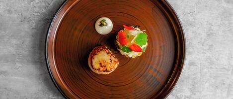 A round, dark brown plate with a grilled item and a small salad on a textured gray surface.