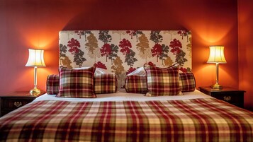 A bed with a plaid bedspread, multiple pillows, and a headboard with a tree pattern. There are two bedside lamps on either side of the bed.