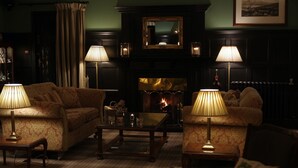 A cozy lounge area with two sofas, a coffee table, and two lamps. A fireplace with a mirror above it is visible, and a framed picture hangs on the wall. - Bunchrew House Hotel (Inverness)