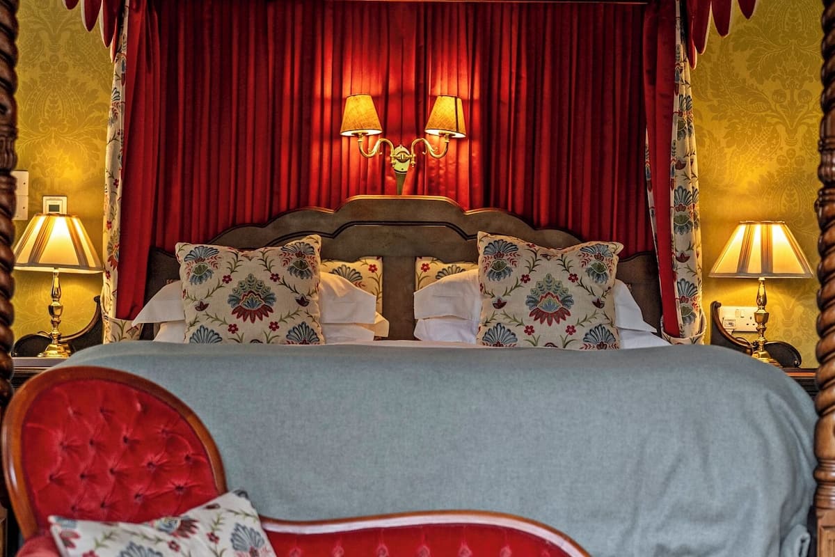 A four-poster bed with red curtains, floral patterned pillows, and two bedside lamps.