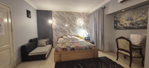 A bedroom with a bed, a sofa, a desk, and a chair.