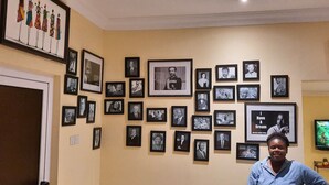 Ein Zimmer mit einer Wand voller gerahmter Fotografien, einem Fernseher und einer Tür.