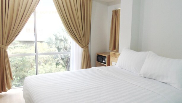 A hotel room with a bed, curtains, a nightstand, and a window with a view of greenery. - An Hotel Jakarta (Jakarta)