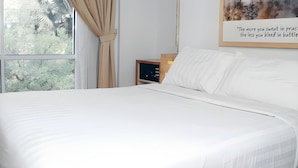 A neatly made bed in a room with a large window, a chair, and a bedside table. - An Hotel Jakarta (Jakarta)