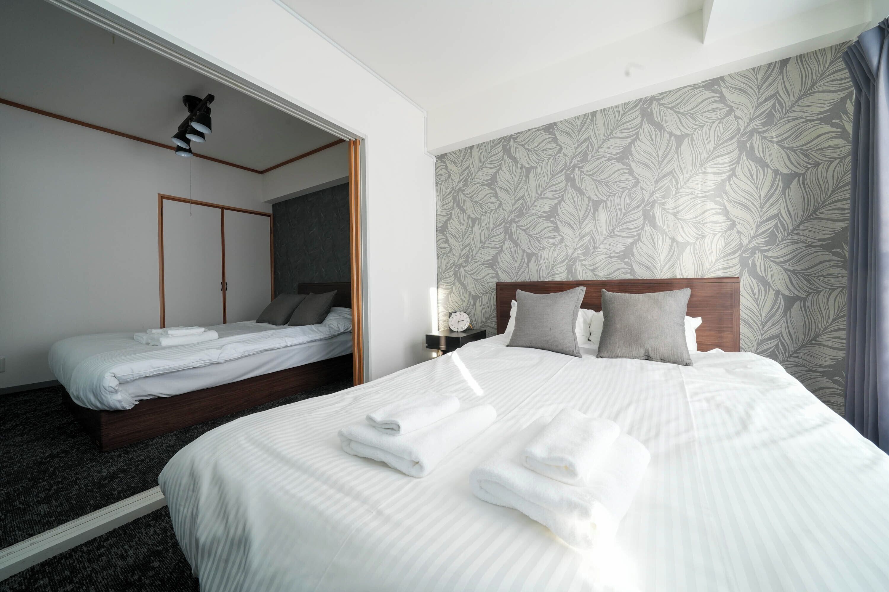 Une chambre d’hôtel avec un grand lit, un lit plus petit, une armoire, une table de chevet avec une lampe et un miroir.