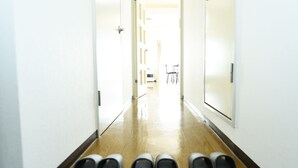 Un passadís amb sòl de fusta i parets blanques que condueix a una habitació amb una cadira i una taula.
