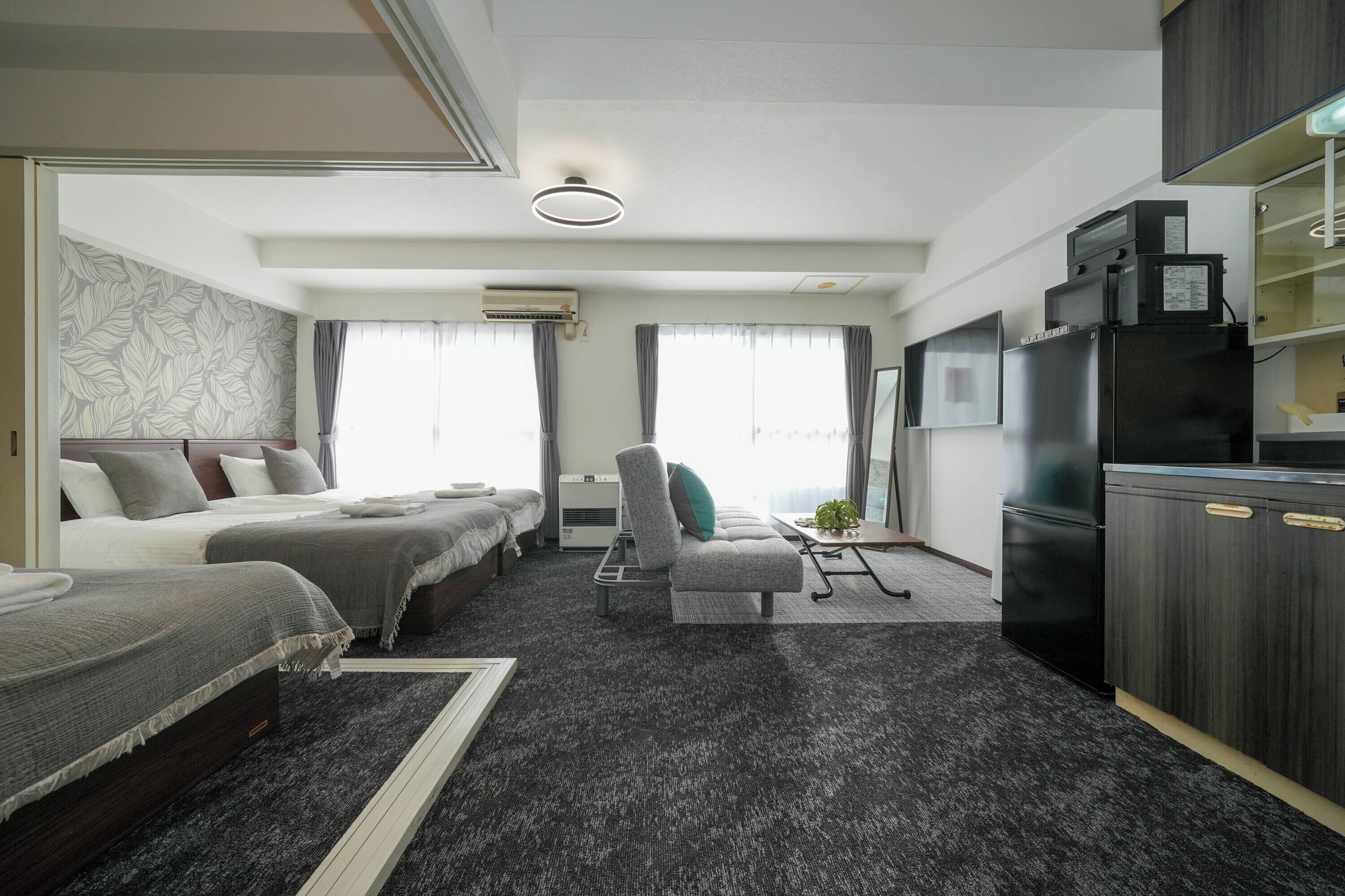 A hotel room with a bed, a chair, a desk, and a kitchenette.