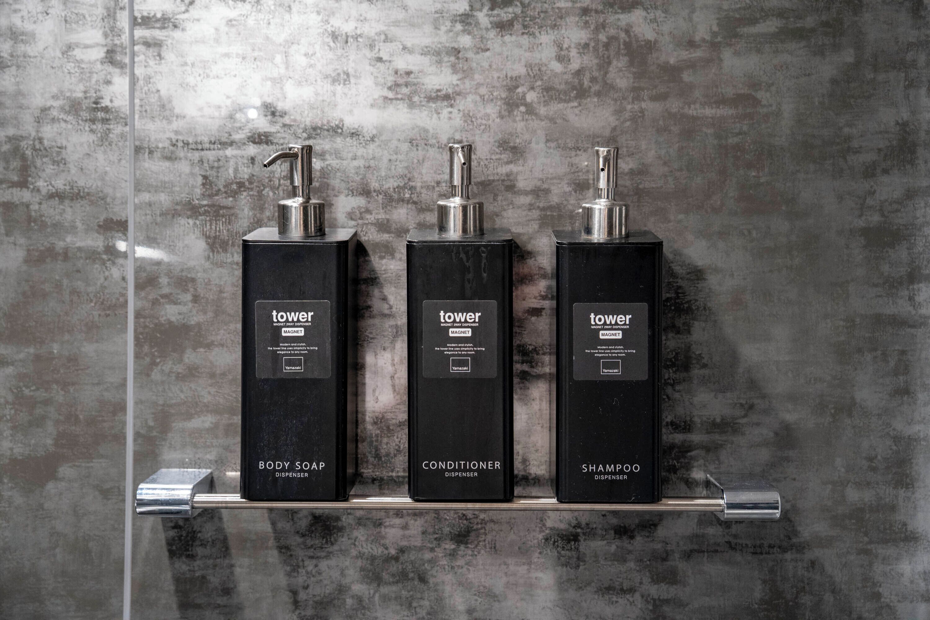Three black dispensers labeled 'tower' on a metallic shelf against a textured wall.