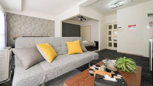 Habitació d'hotel moderna amb un sofà gris, coixins grocs, una taula de centre de fusta i una planta en test.