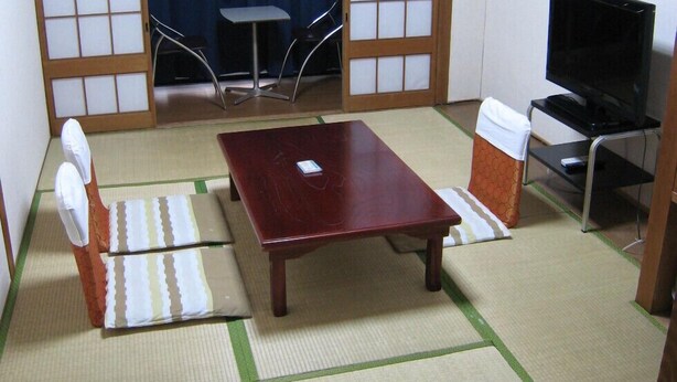 A traditional Japanese room with tatami flooring, a low table, a television, and a futon bed. - Hotel Eco Dogo (Matsuyama)