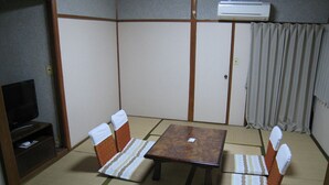 A tatami mat room with a low table and four chairs, a television, and an air conditioning unit. - Hotel Eco Dogo (Matsuyama)