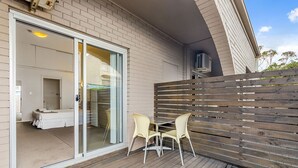 A room with a sliding glass door leading to a bathroom, a wooden deck with two chairs, and a wooden fence. - Nova Kiama (Wollongong)