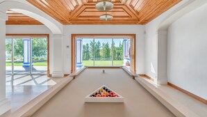 Mesa de billar con bolas en una habitación con techo de madera y ventanas amplias.