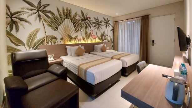 A hotel room with two beds, a desk, a chair, and a large wall mural of tropical plants. - Doho Homestay (Jember)