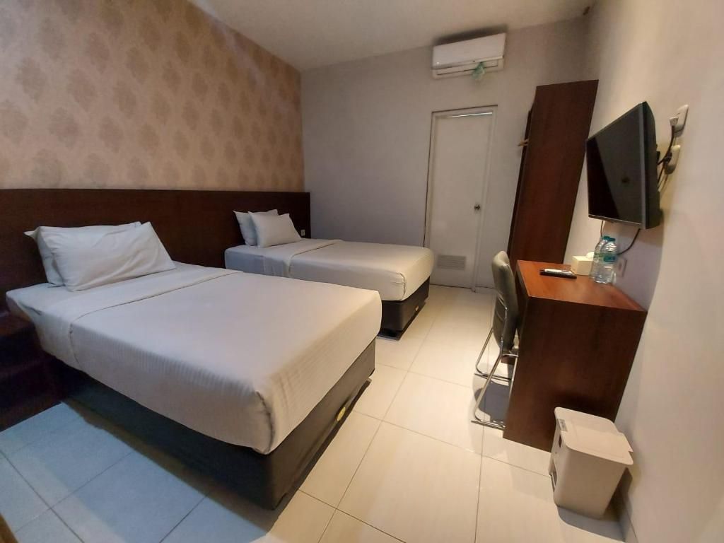 A hotel room with two beds, a desk, a chair, a television, and a trash bin.